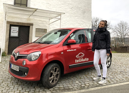 Studentin vor rotem Auto mit Schriftzug 